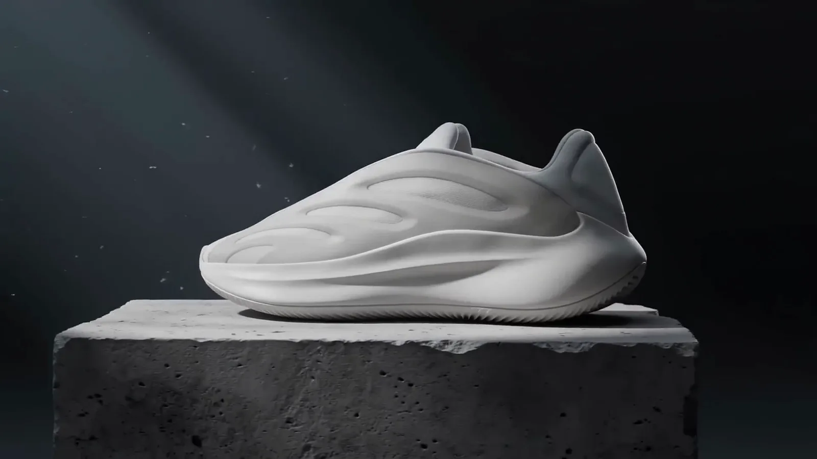 A white sneaker on a rough concrete plinth under hard side light, with dust floating in the dark